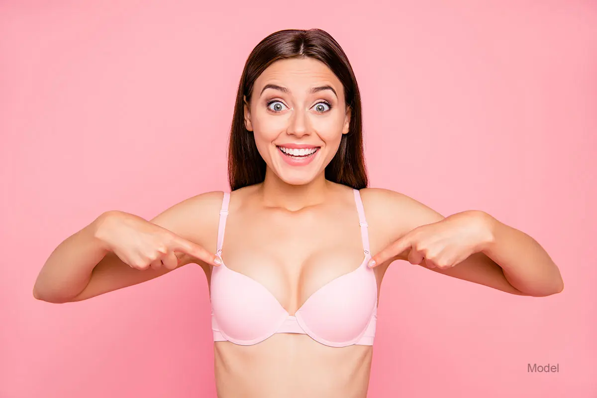 A pretty woman wearing a bra, happily points at her breasts
