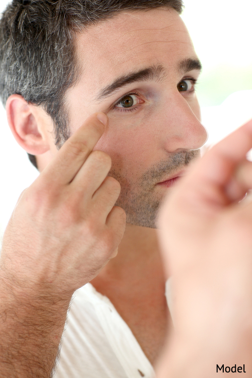 Man looking at wrinkles in mirror, considering a plastic surgery procedure.