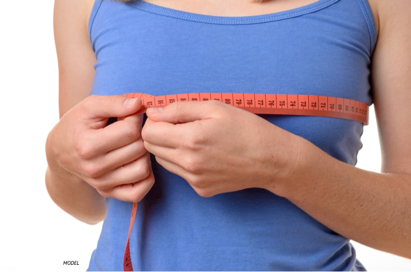 Woman wearing blue shirt measuring her breasts.