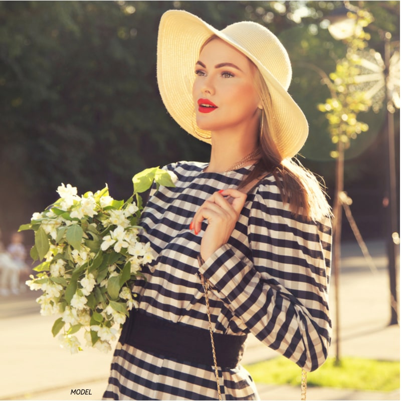 A pretty woman walking in summer wearing a hat and carrying flowers.