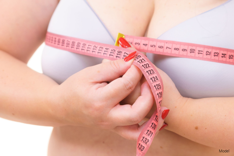 A woman wearing a white bra uses a measuring tape to measure her breasts.